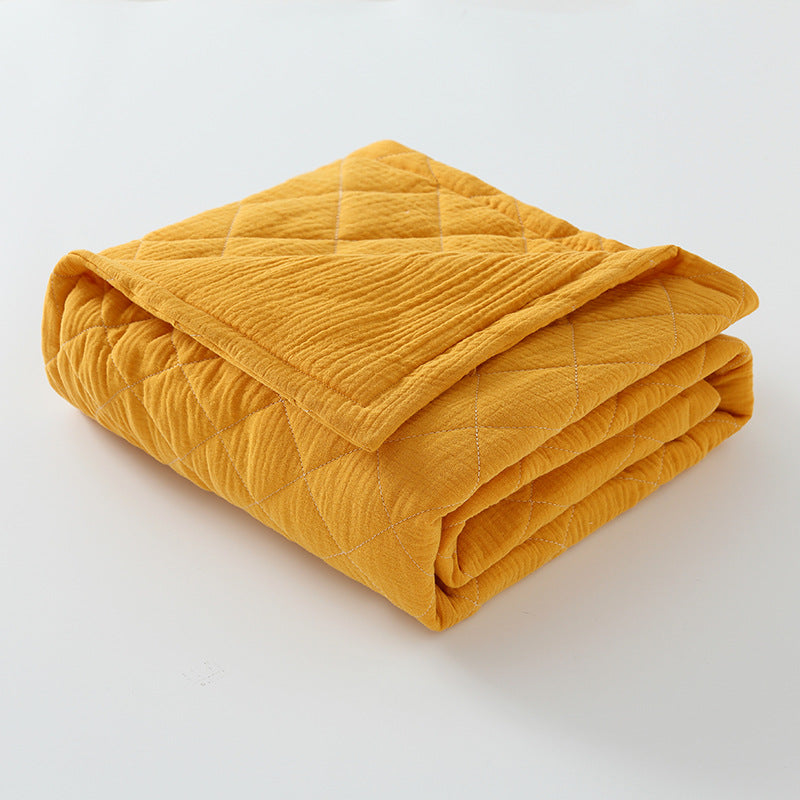 Mustard yellow cotton muslin baby quilt folded with lightweight padding and diamond stitching