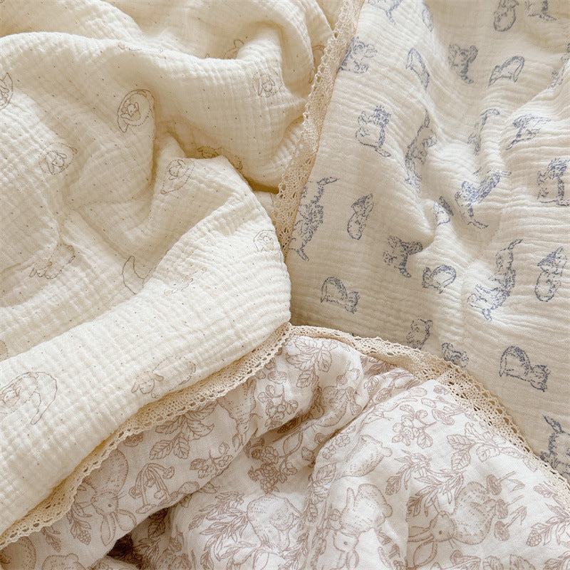 Close-up of lamb, kitty, and woodland animal themed comforter prints on soft cotton muslin, detailed with lace edge.
