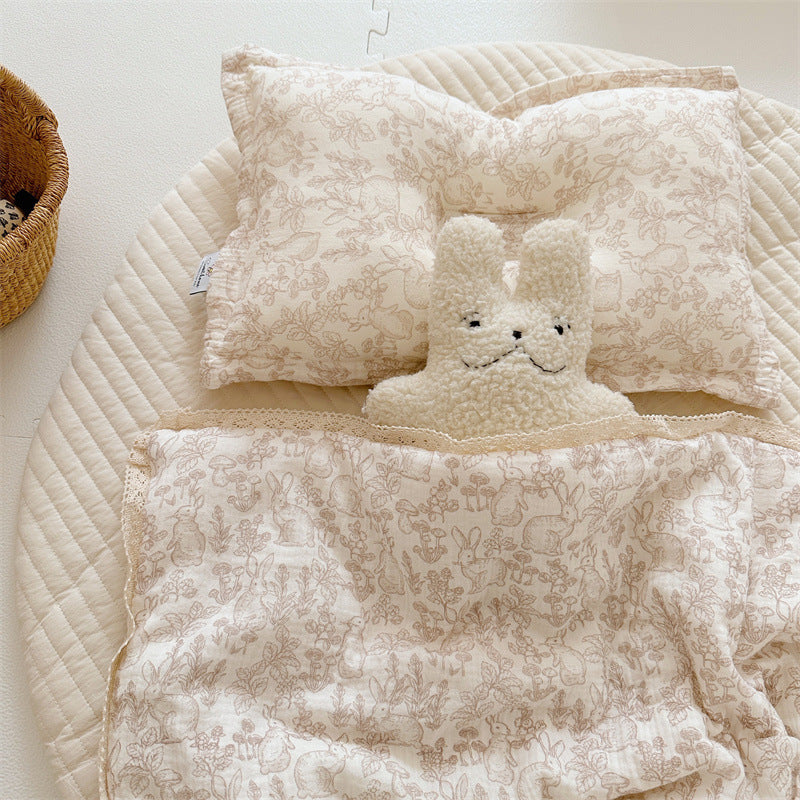 Woodland animal print comforter and pillow in beige tones, styled with plush bunny toy on a round padded mat
