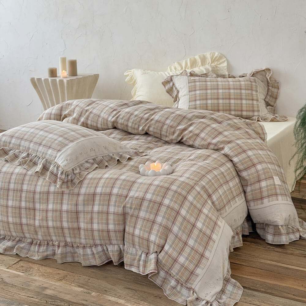 Beige plaid ruffle bedding set styled on a bed in a cozy, light-filled room with candles on a side table