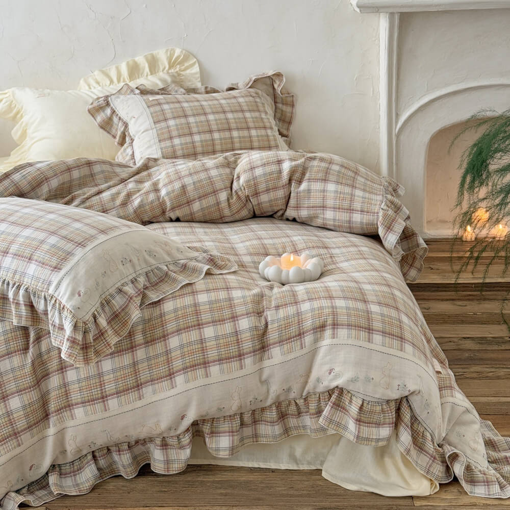 Plaid cotton muslin bedding set with ruffled edges, arranged on a bed near a white fireplace for a soft cottage look