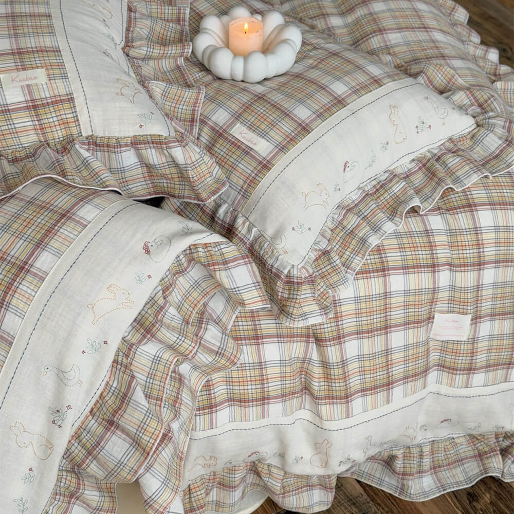 Close-up of beige plaid bedding set, highlighting the ruffled edge and delicate bunny and duck embroidery on soft cotton muslin fabric