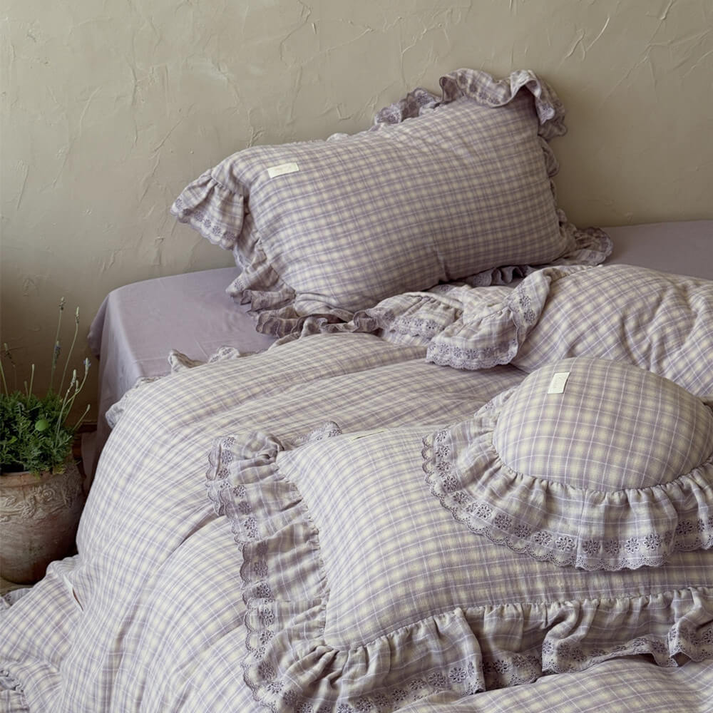 Top-down view of lavender plaid bedding and pillows with book and candle