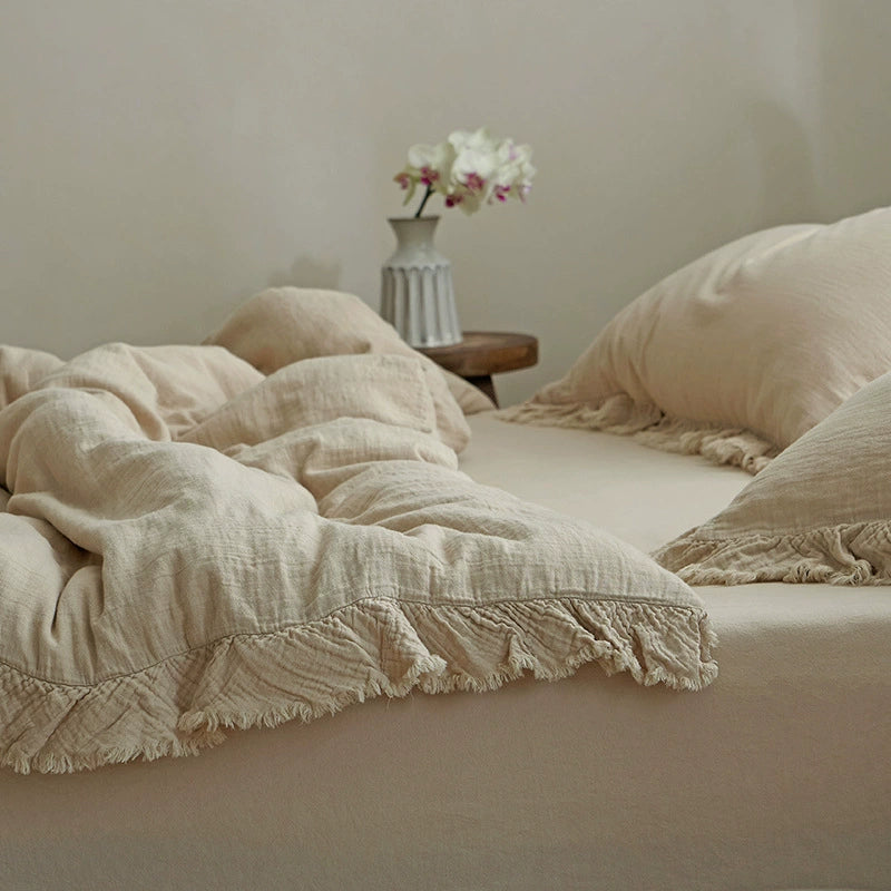 A close-up of a khaki cotton gauze duvet cover and a pillow with a distinct fringe border, displaying the fabric's soft, wrinkled texture.