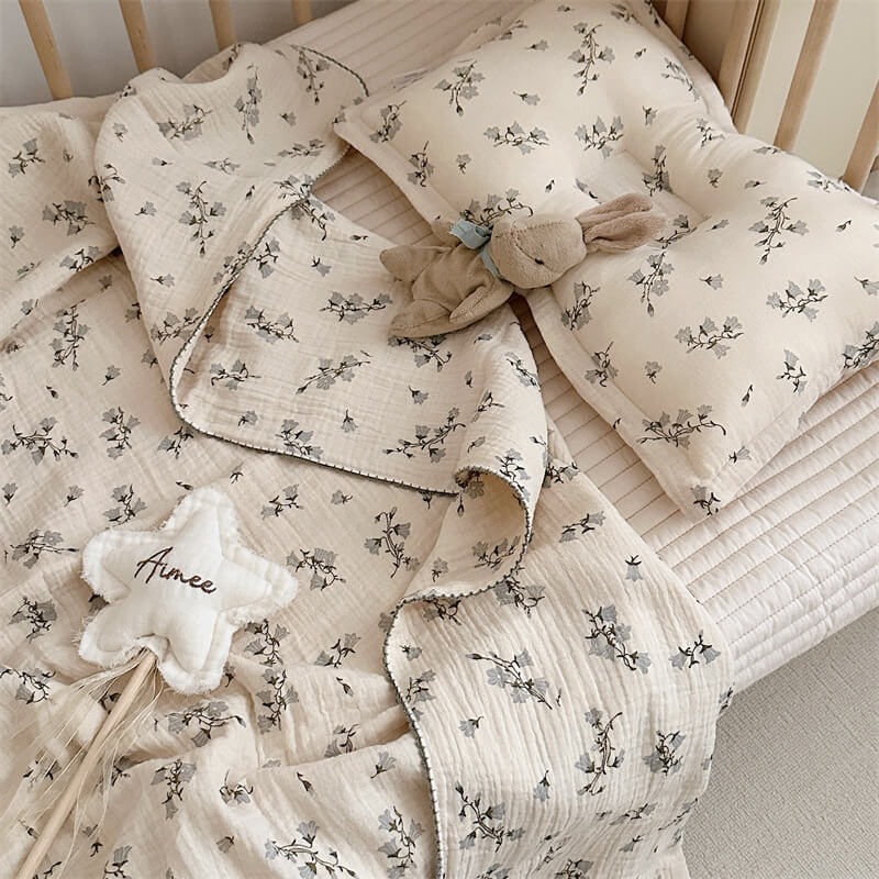 A cozy Hyacinth Floral muslin toddler blanket and pillow set, 47"x51", styled in a crib with a plush rabbit toy and a star-shaped plush toy.