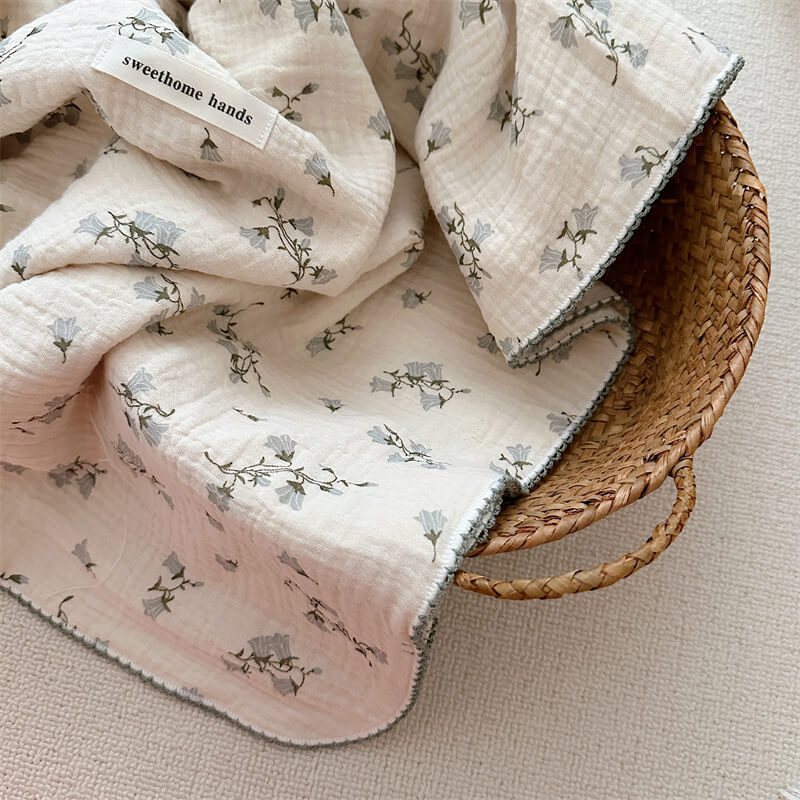 A detailed photo of the Hyacinth Floral muslin toddler blanket, folded over the edge of a woven basket, emphasizing its soft, lightweight fabric and delicate pattern.