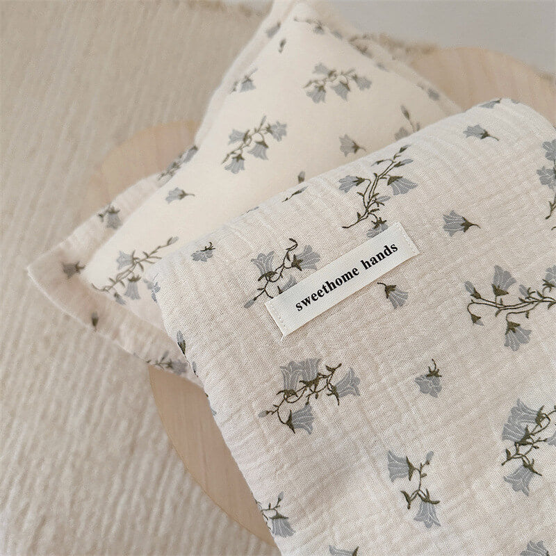 A close-up shot of the Hyacinth Floral muslin blanket and pillow set, highlighting the detailed blue flower print.