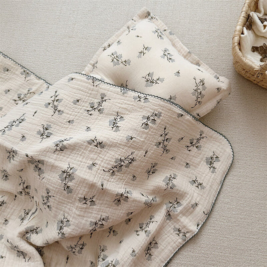 A full view of the Hyacinth Floral muslin toddler blanket and pillow set, featuring blue flower clusters, laid out on a light-colored rug.