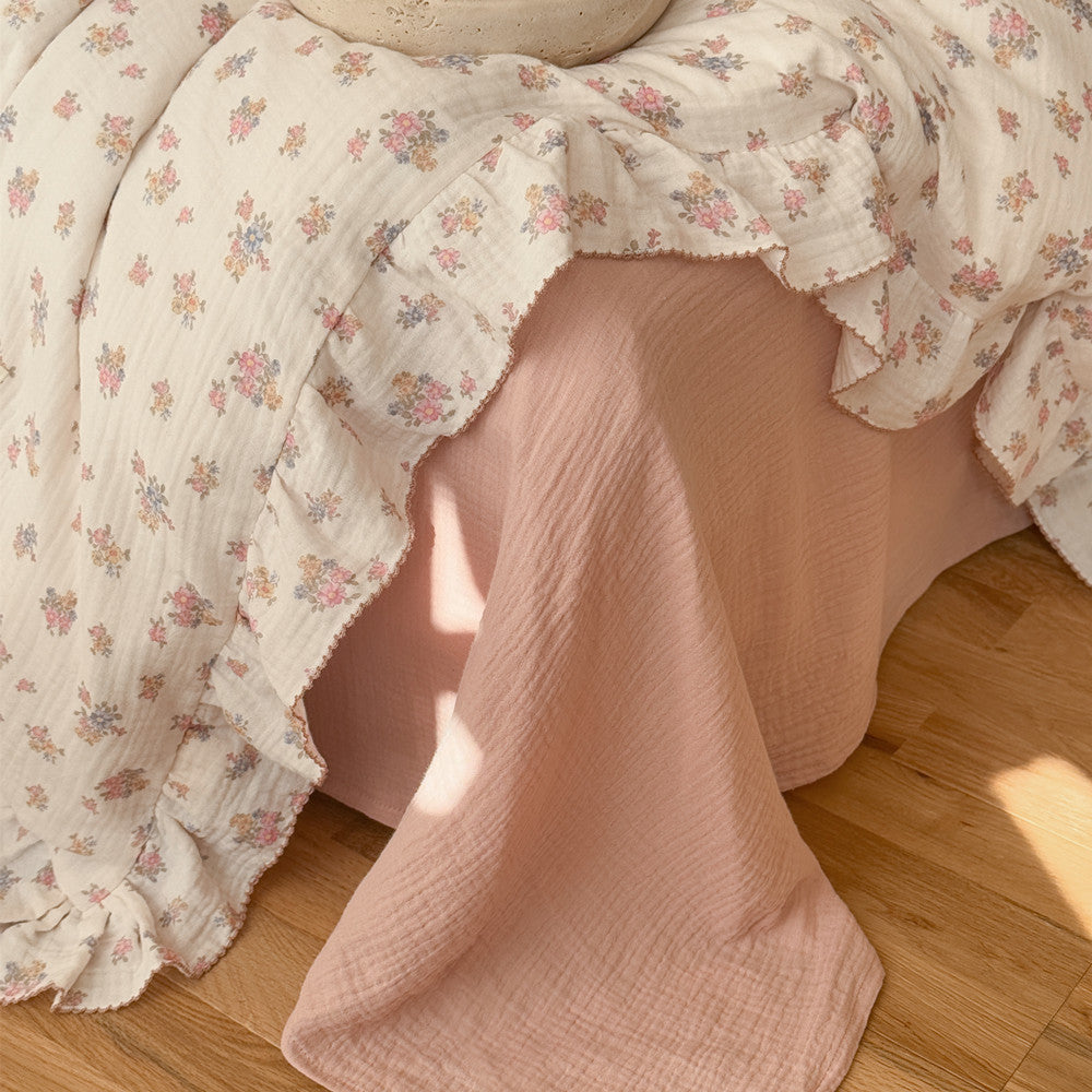 Close-up detail of the Tuberose Floral Muslin Duvet Cover's ruffled trim and delicate floral print, draped over a solid pink muslin flat sheet, emphasizing the soft texture.