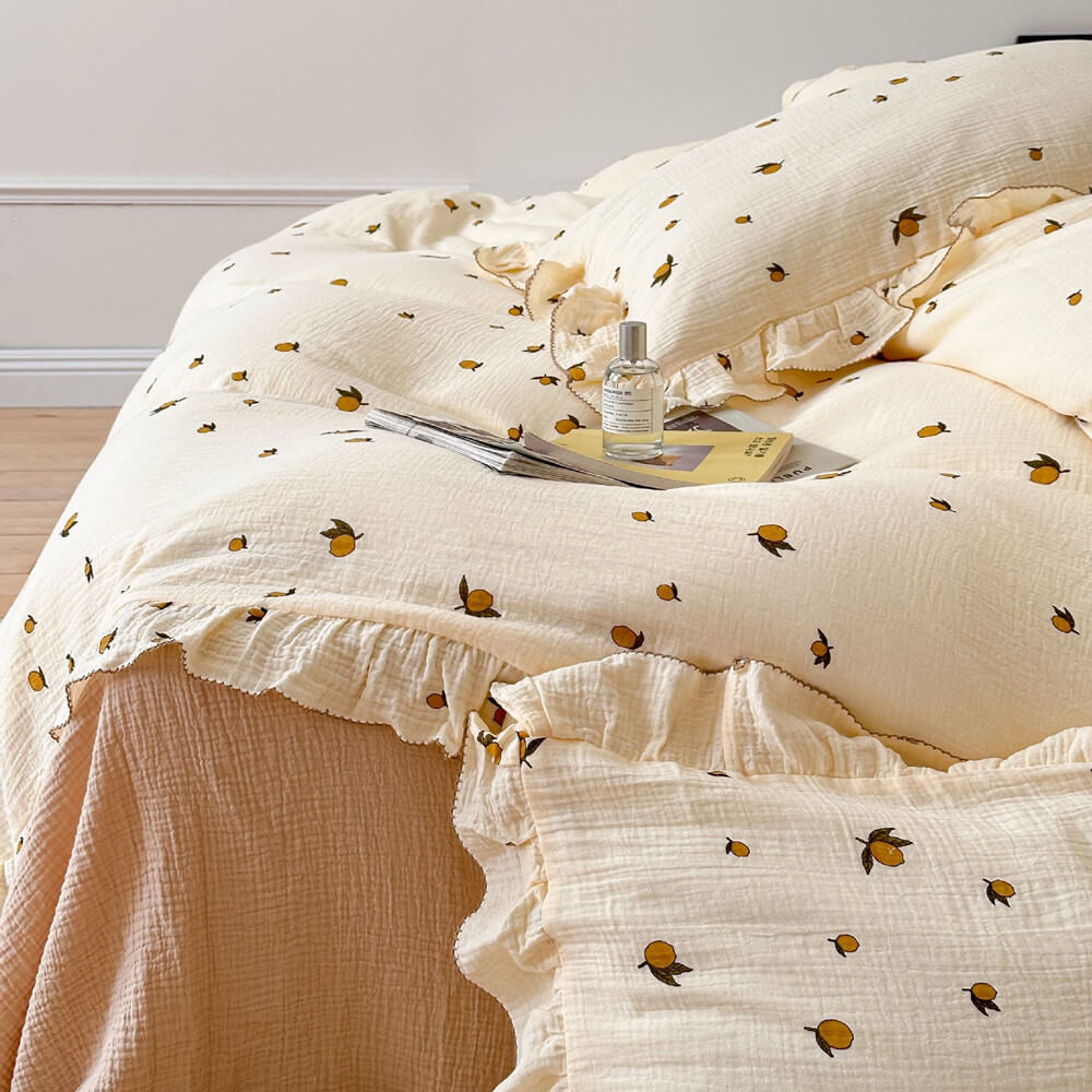 A close-up of the Zesty Lemon cotton muslin duvet cover set on a queen-size bed, showing the detailed lemon print and ruffled edge