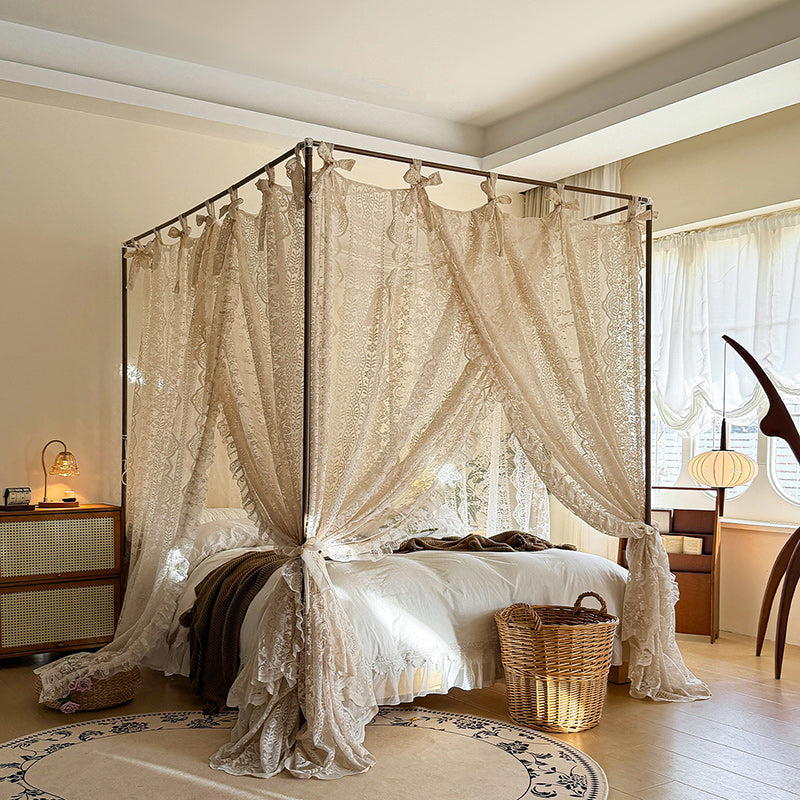 Bedroom with a canopy bed draped in lace curtains, wooden nightstands, and a lamp.