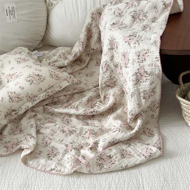 Rosebud pink floral cotton muslin baby blanket draped on a bed