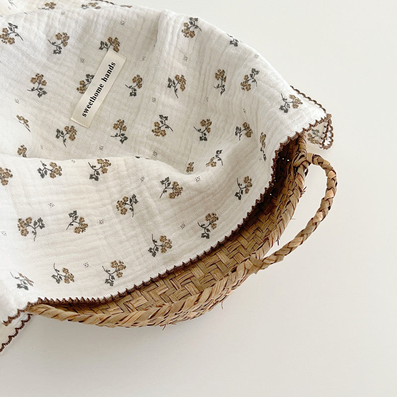 A close-up of a corner of the Calendula Floral muslin blanket, showing the delicate ochre blossoms and charcoal stems on the crinkled fabric.