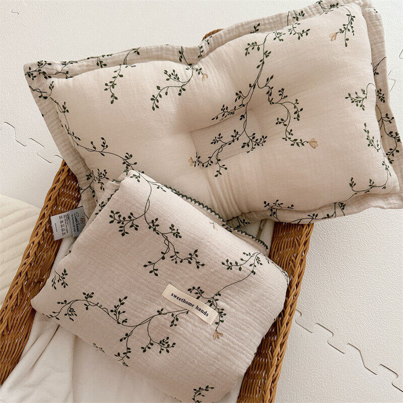 The Botanical muslin toddler blanket and pillow set, featuring a delicate green vine pattern, folded in a woven basket.