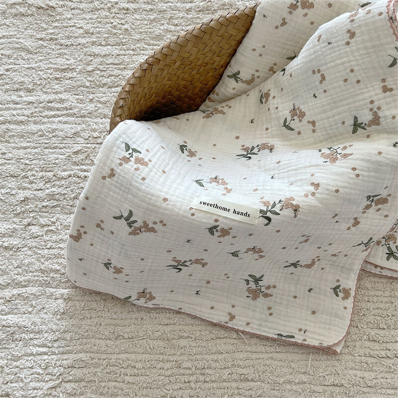 Laurel floral muslin baby blanket folded in a woven basket on a textured rug.