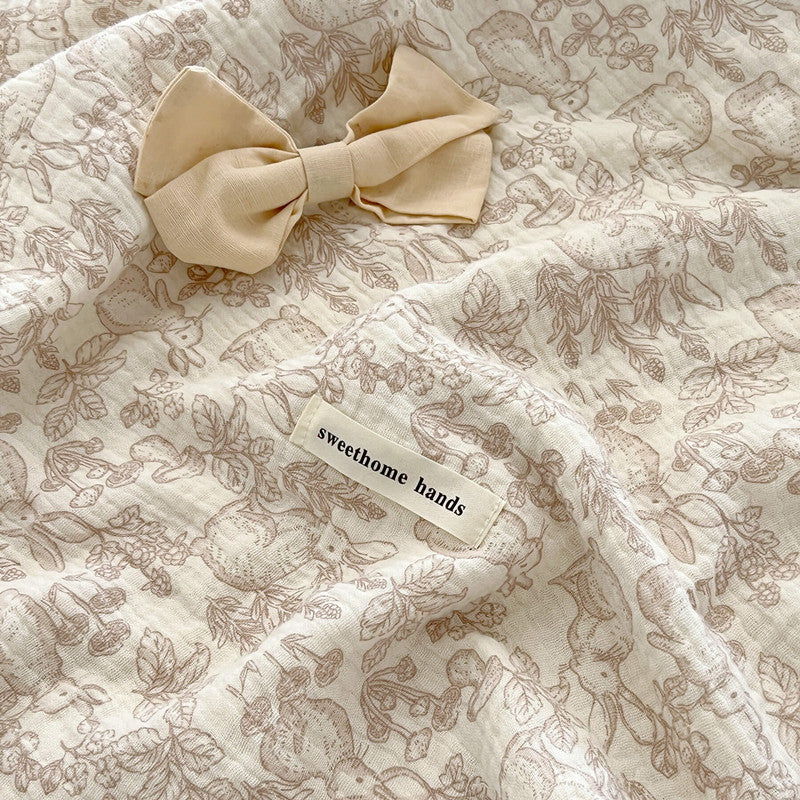 Close-up of a Dreamwoods floral cotton muslin blanket with a ribbon bow on top, a great size for use as a stroller blanket.