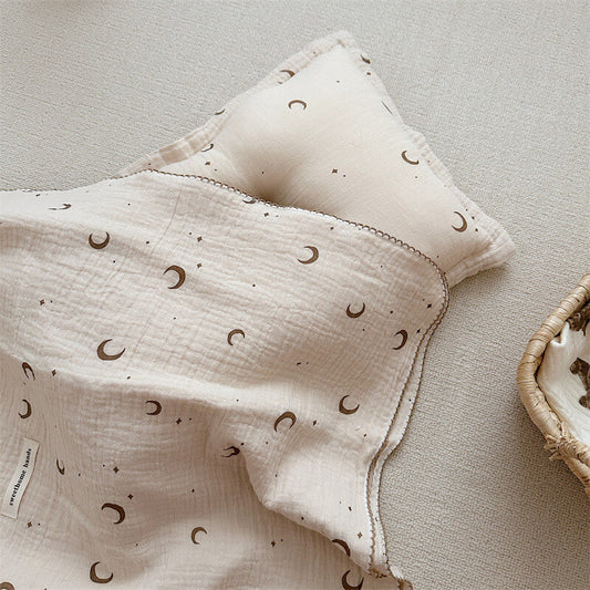 Overhead view of a brown moon and star muslin blanket and pillow set displayed on a rug