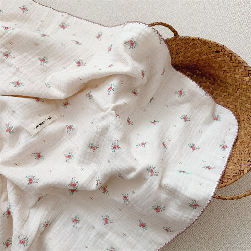 An affordable baby girls blanket and pillow set, featuring a Tiny Rose floral pattern, draped inside a rustic woven basket on a soft carpet.