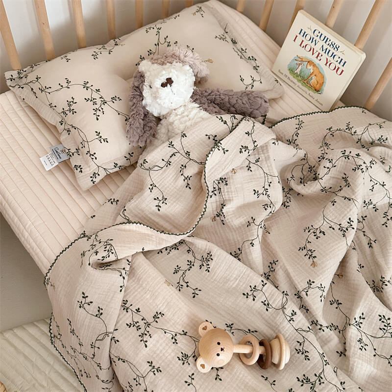 A cozy crib scene featuring the Botanical muslin blanket and pillow set, a plush bunny toy, and a wooden rattle.