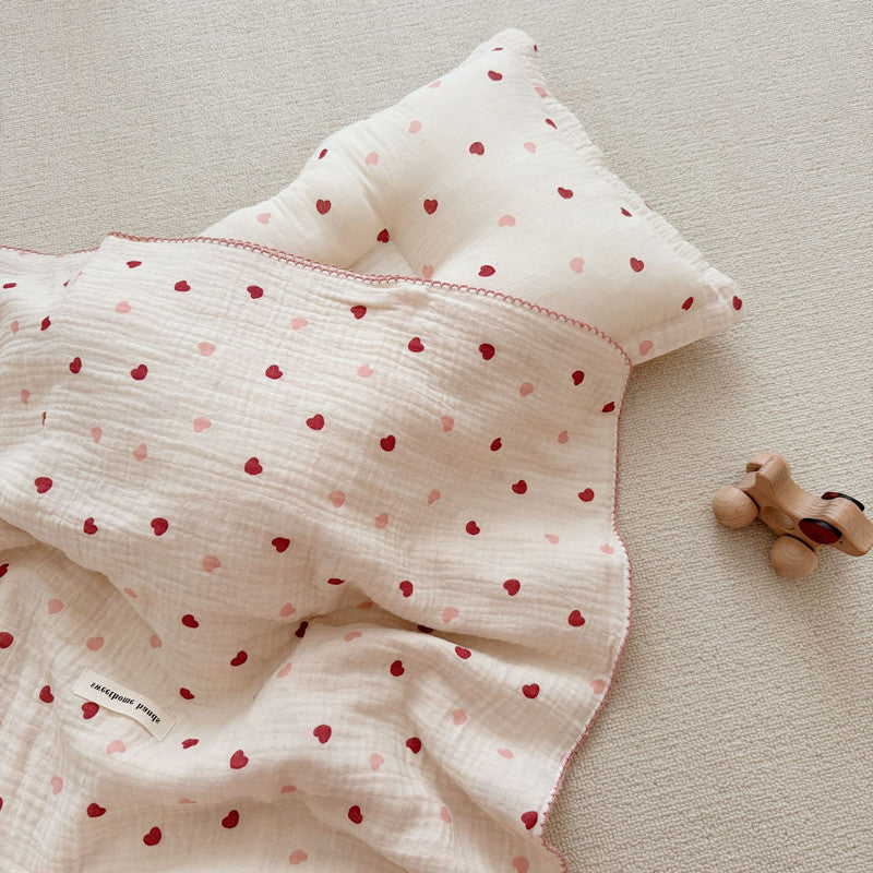 A close-up, top-down view of the Pink and red Heart muslin blanket and pillow set, emphasizing the soft, multi-colored heart pattern and crinkled texture.