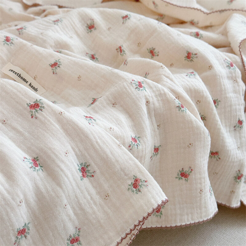 A close-up shot of a soft muslin blanket from the Tiny Rose collection, showing the delicate flower pattern and the brand's label.