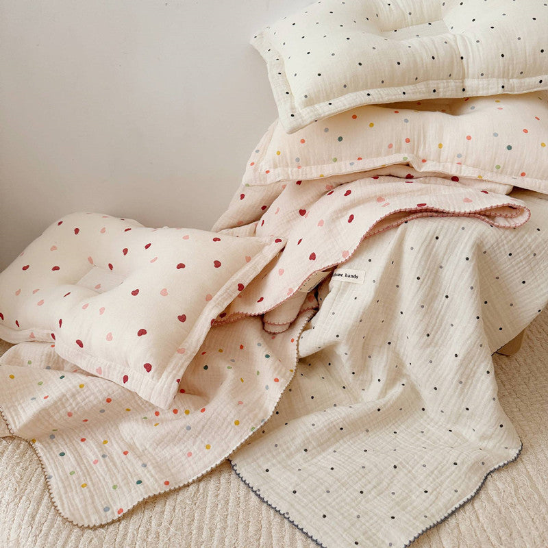 A pile of muslin blankets and pillows, featuring the Pink Heart pattern on the top layer, alongside other designs like colorful dots and polka dots
