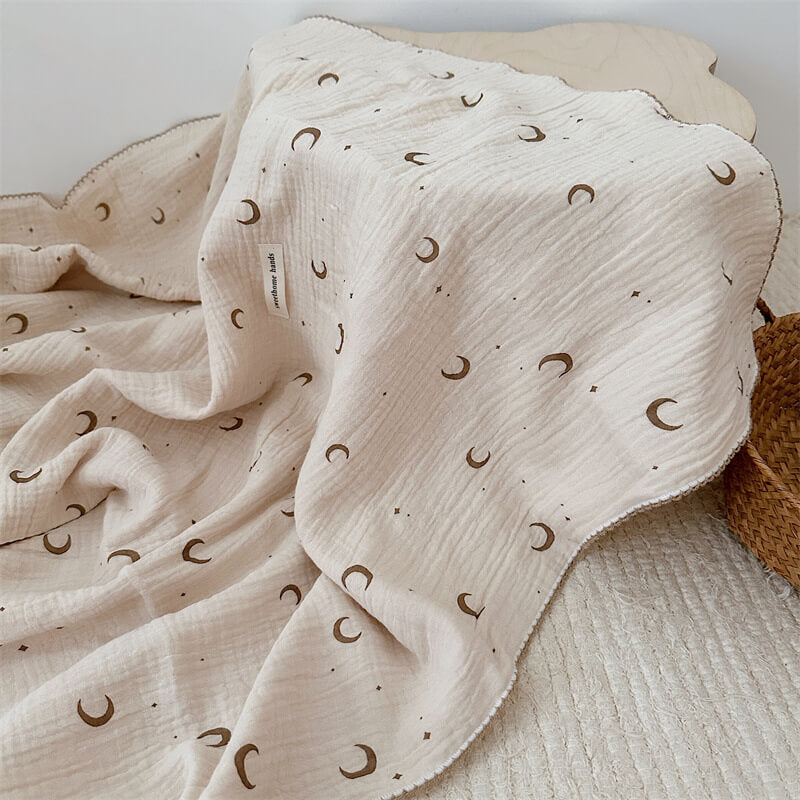Soft brown moon and star print muslin toddler blanket with a scalloped edge, perfect for a baby girl's nursery.