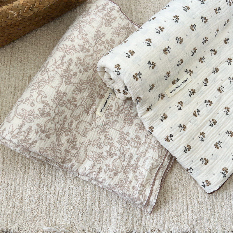 The Calendula Floral muslin blanket in a half-rolled, half-open position on a white surface, showcasing the full pattern and the soft, breathable texture.