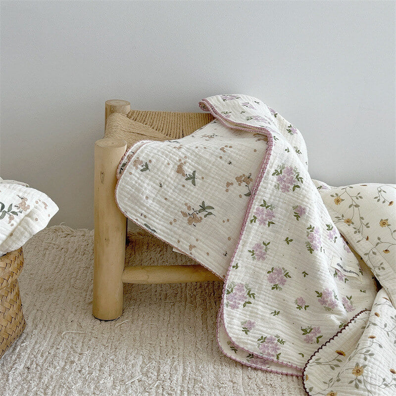 Laurel floral muslin baby blanket draped over a wooden stool, with a matching pillow nearby.