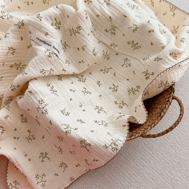 Close-up of a soft muslin baby receiving blanket with an olive green floral print, naturally crinkled texture