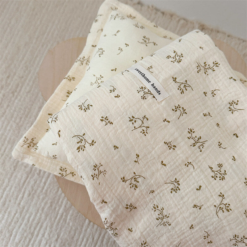 Stacked view of a muslin baby receiving blanket and matching pillow, highlighting the subtle olive green floral print and fabric texture