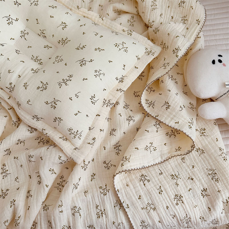 Overhead shot of a baby swaddle blanket and pillow set, showcasing the olive green floral pattern and scalloped edges.