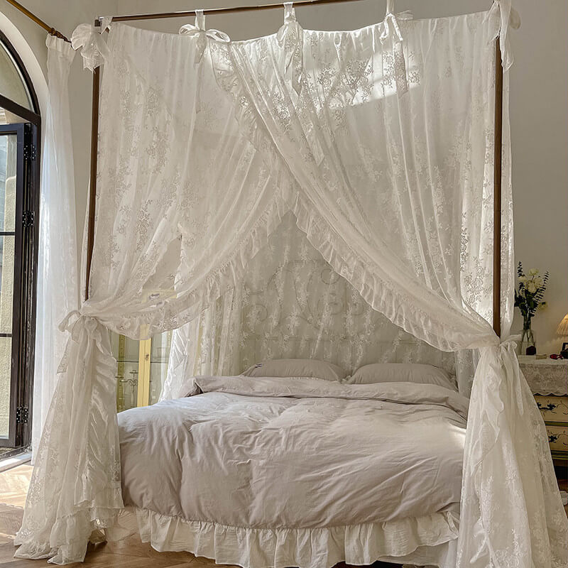 A cozy bedroom scene featuring a white floral lace bed canopy with ruffle trim, tied back on a wooden 4-poster bed. The room has natural light and the bed is made with light-colored bedding.