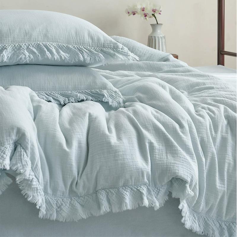 A close-up view of the light blue cotton gauze bedding set, focusing on the crinkled texture and the fringe details on the duvet cover and pillow shams.