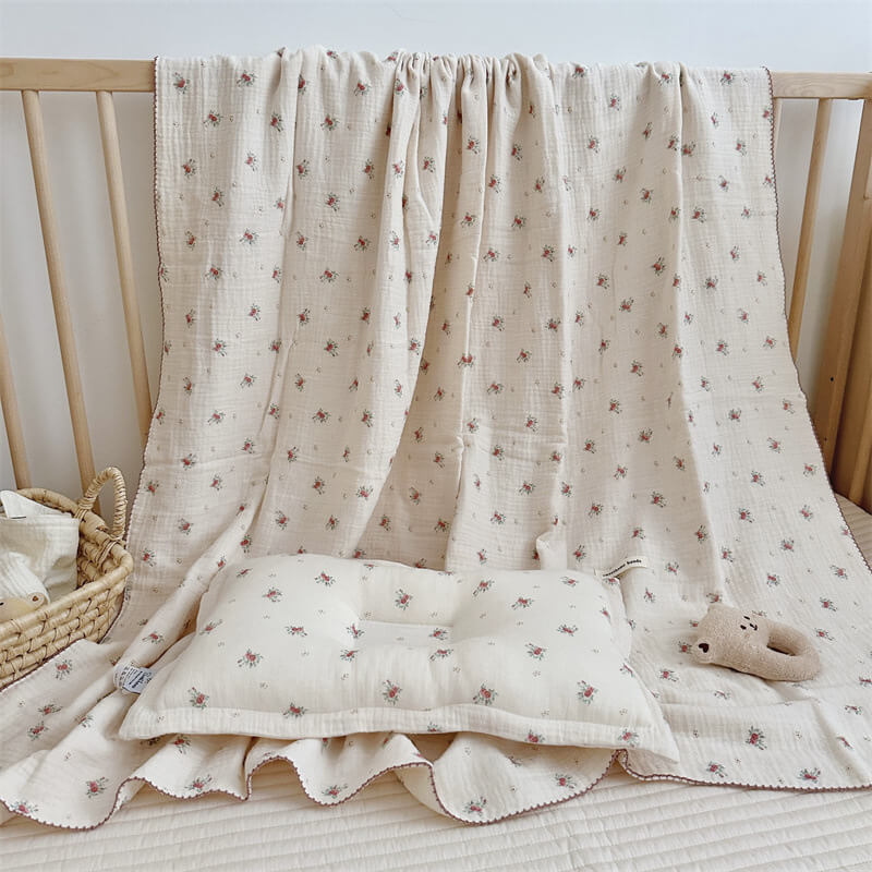 A high-quality Tiny Rose Muslin Toddler Blanket & Pillow Set for baby girls displayed in a wooden crib, showcasing a lightweight, floral design.