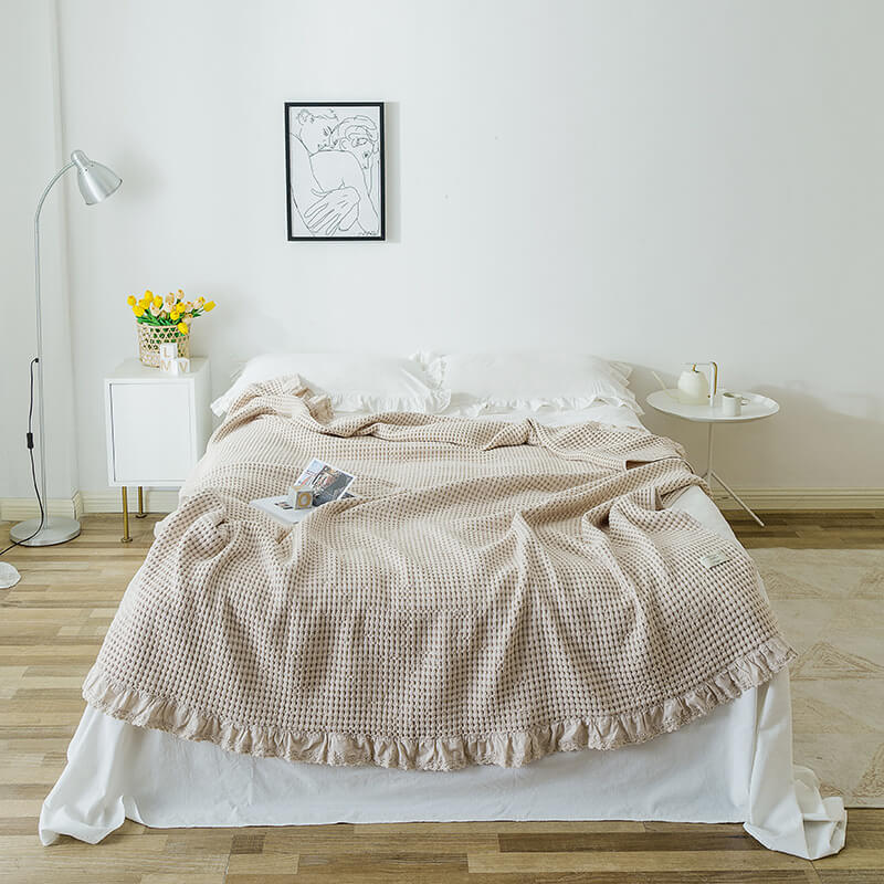 Beige cotton waffle blanket with ruffle edge displayed on a bed