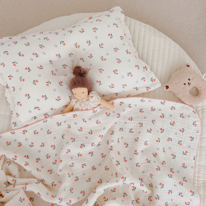 A top-down shot of the Tulip Floral baby pillow and blanket, with a doll and bear-shaped toy, creating a cozy and inviting nursery scene.