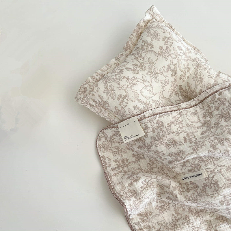 A soft Dreamwoods floral muslin baby blanket and a matching pillow on a white surface, a great swaddle for a newborn.