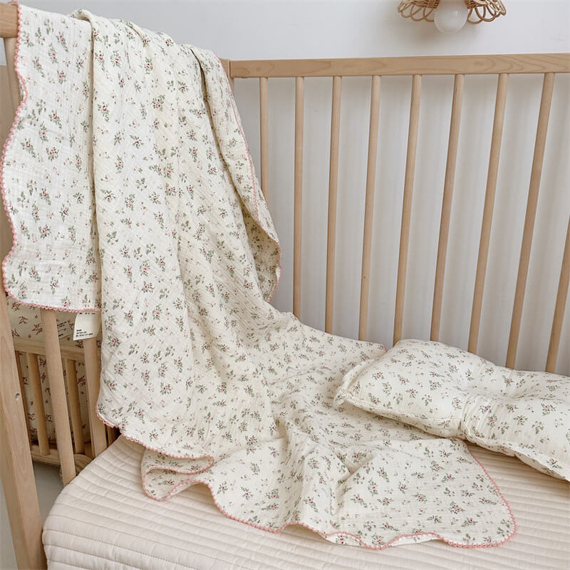 A close-up shot of the Pomegranate Floral muslin blanket and pillow set, highlighting the vibrant red flowers and grey leaves on the lightweight, crinkled fabric.