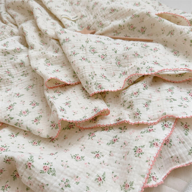 A detailed flat lay of the Pomegranate Floral muslin blanket, showcasing the intricate design of pinkish-brown flowers and green leaves with a white background.
