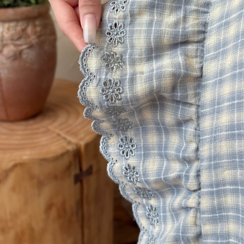 Detailed close-up of cotton muslin blue plaid bedding with embroidered lace ruffle