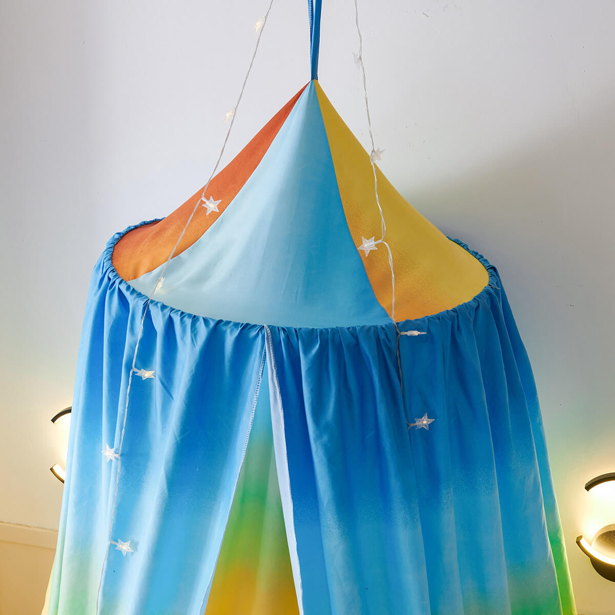 Close-up of a rainbow bed canopy showing the colorful fabric and star-shaped string lights.