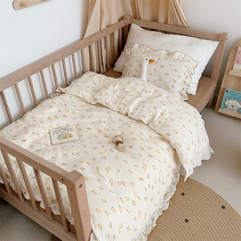 Duckling print cotton muslin bedding set neatly arranged in a wooden toddler bed