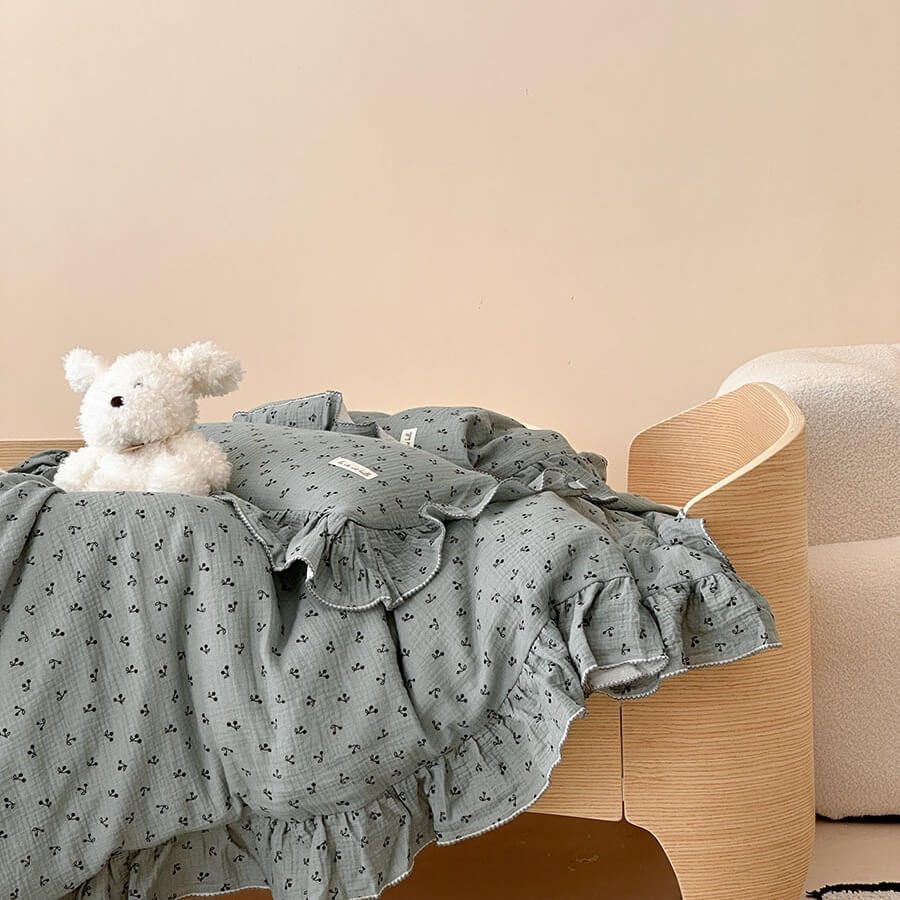 Sage floral cotton gauze kids bedding set on a wooden bed, featuring ruffled duvet cover and matching pillow shams.