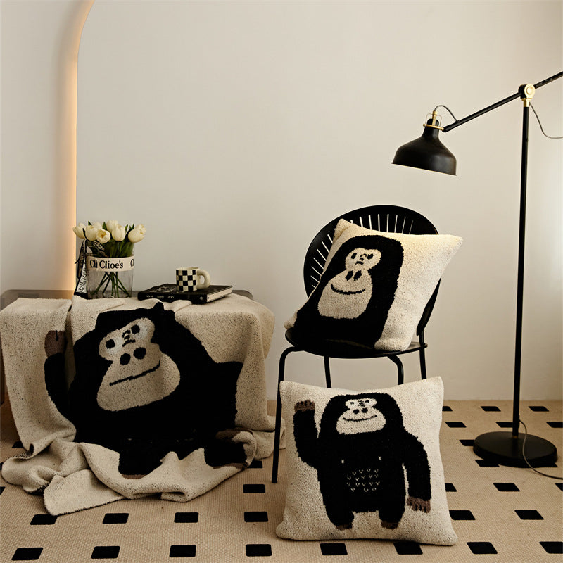 A set of chimpanzee throw blankets and pillowcases with both "Hello" and "Face" designs, styled in a modern living room.