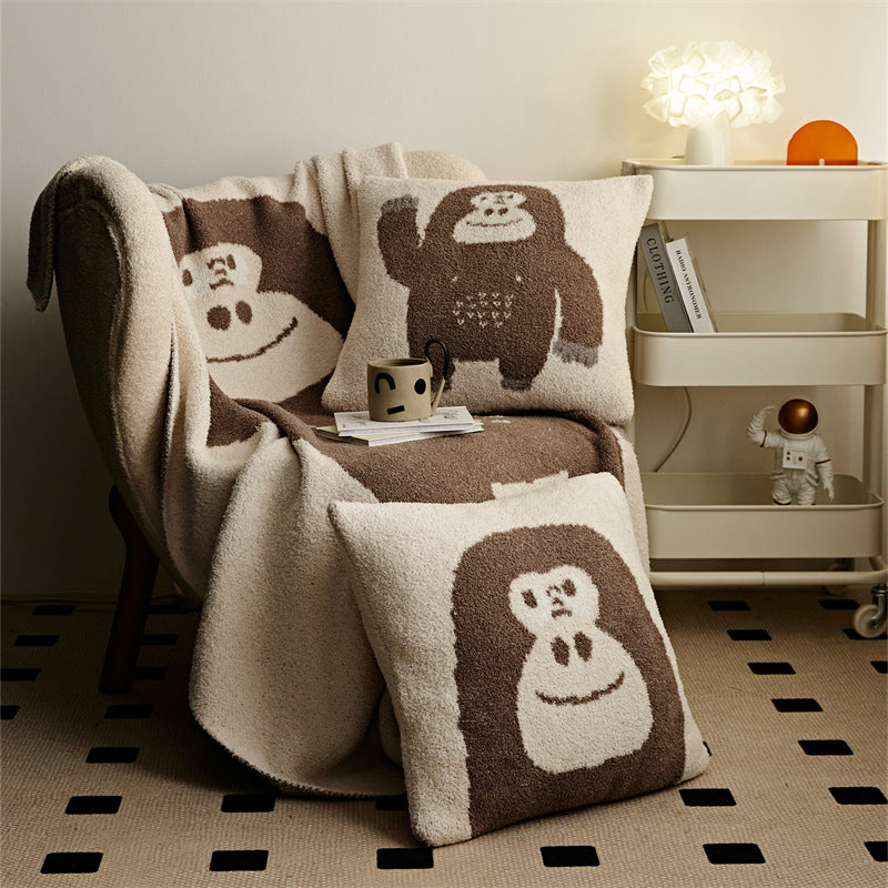 A chimpanzee throw blanket and two matching pillows on an armchair, creating a cute and cozy animal-themed accent