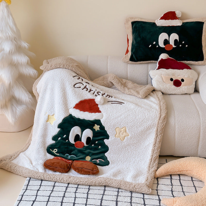 A cozy Christmas sherpa throw blanket with an embroidered Christmas tree character, placed on a sofa with holiday pillows.