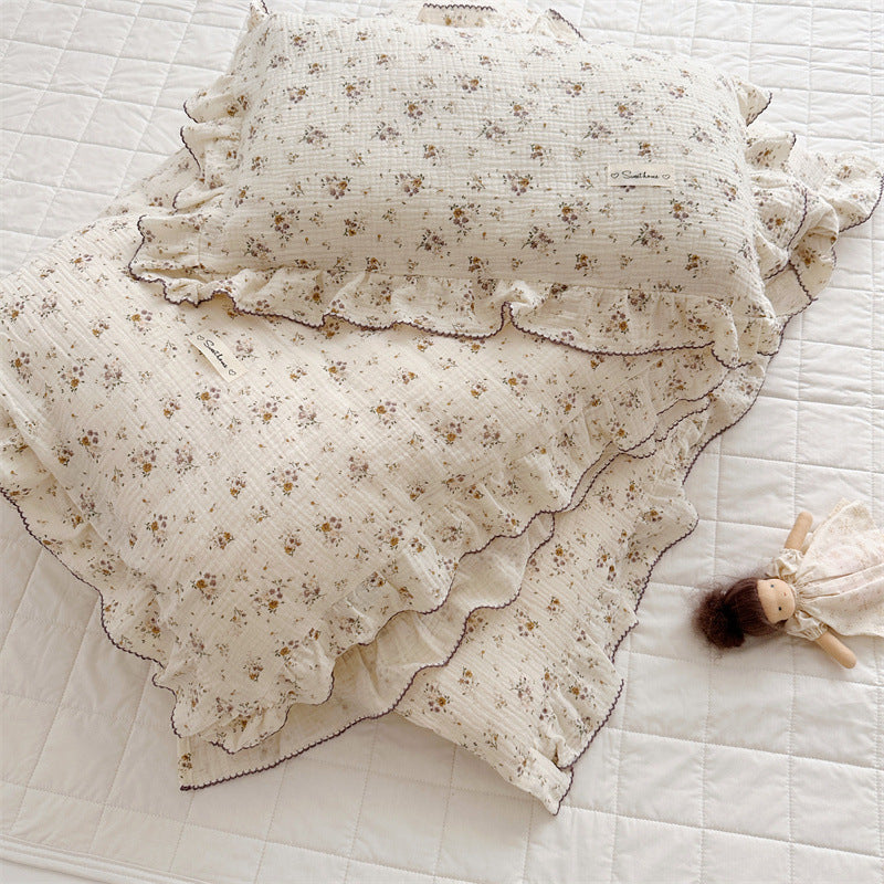 Floral-patterned baby blanket and pillow on a white quilt with a small doll.