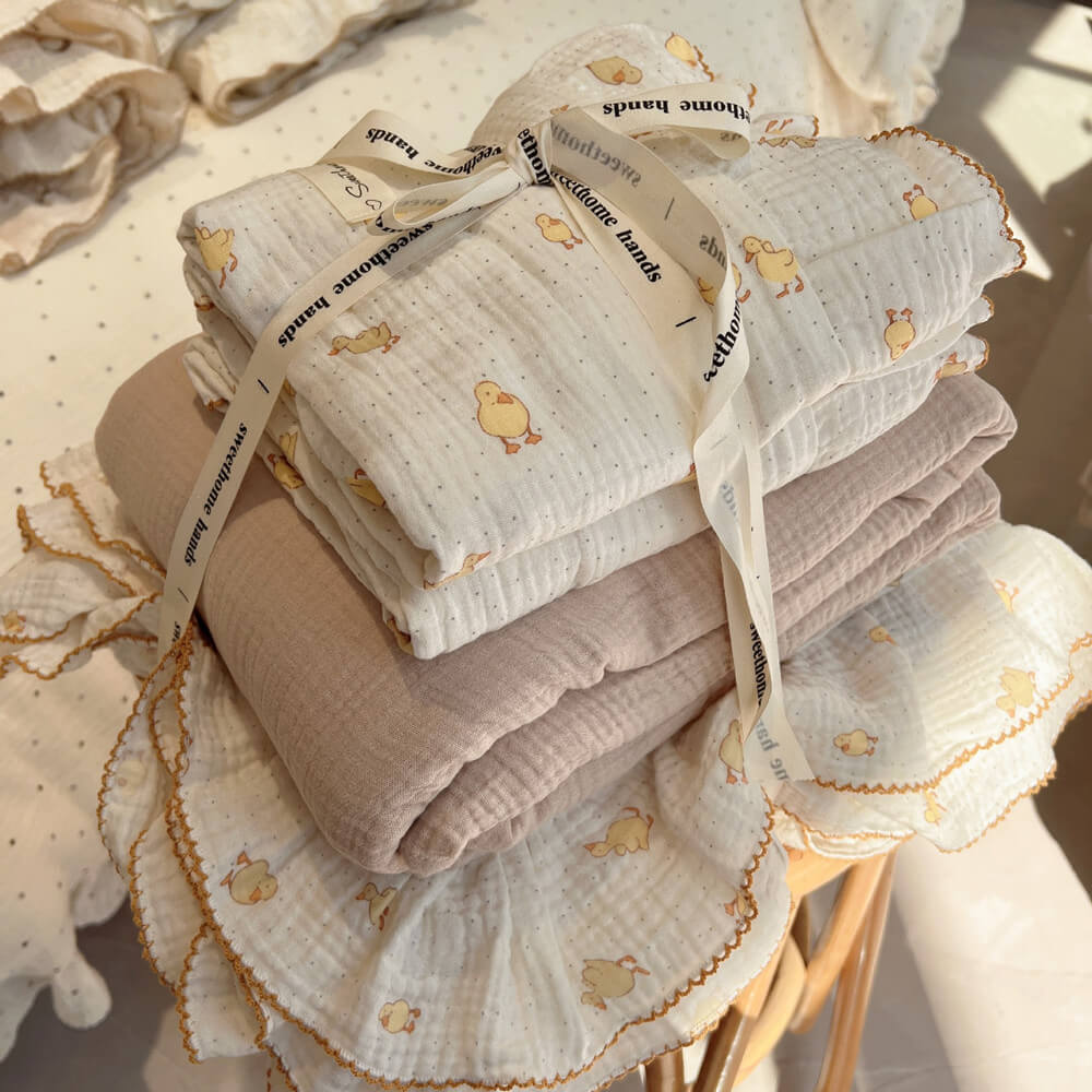 A neatly folded stack of a twin-size cotton muslin duvet cover set with a duckling print and ruffled edges, tied with a ribbon