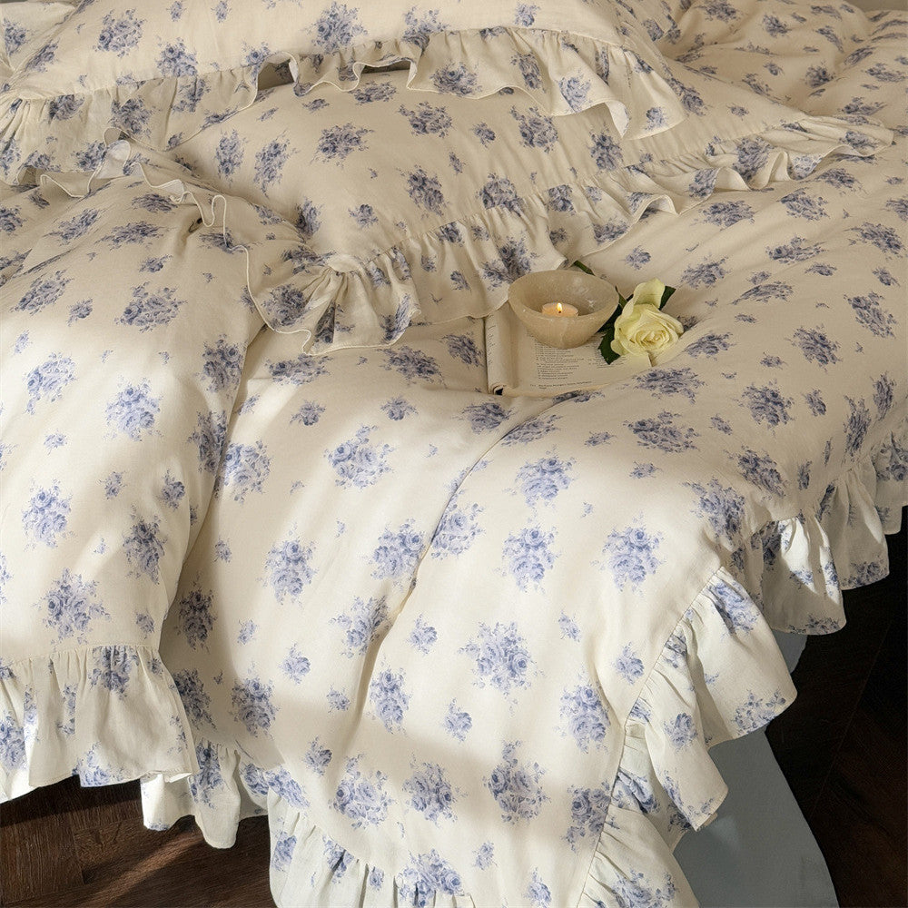 Close-up of a soft and breathable cotton muslin bedding set, featuring a dusty blue floral pattern and romantic ruffle trim on the duvet cover and pillows.